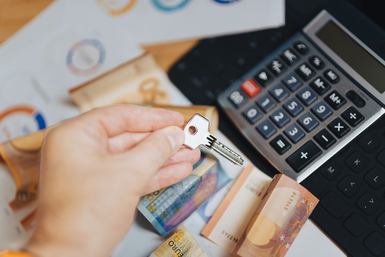Hand holding key above Euro banknotes and calculator, symbolizing real estate investment.