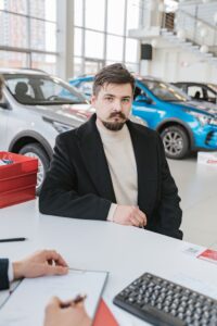 Home A man in a coat discusses with a sales representative in a bright, modern car showroom.