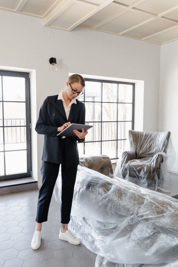 pexels photo 7414909 A real estate agent inspects a modern house with covered furniture, preparing it for potential buyers.