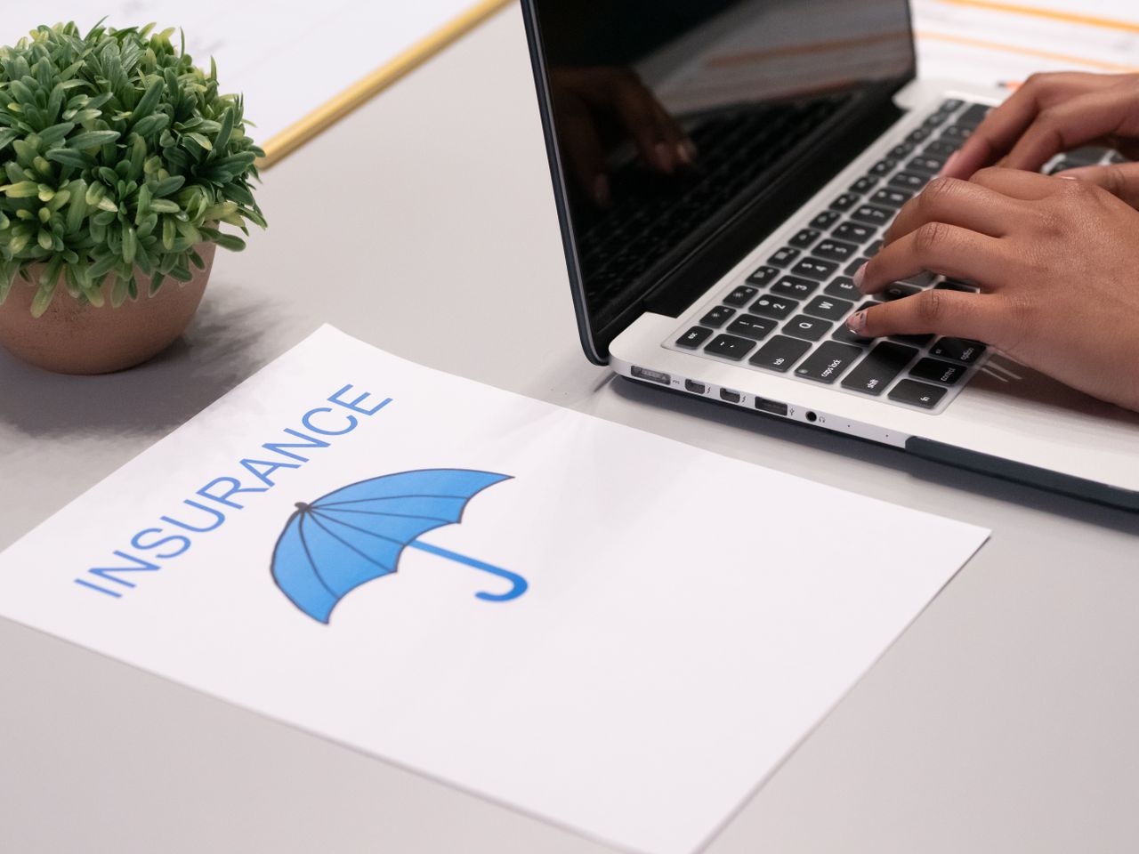 Crafting Captivating Headlines: Your awesome post title goes here Close-up of hands typing on laptop with an insurance document visible on the desk.
